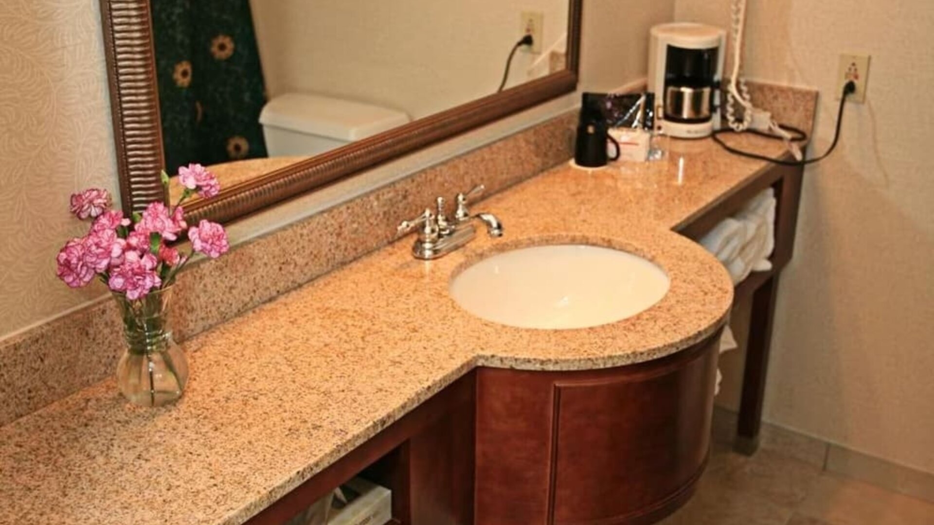 Guest bathroom featuring a granite vanity, large framed mirror, fresh towels, and convenient in-room amenities at Sturbridge Host Hotel.
