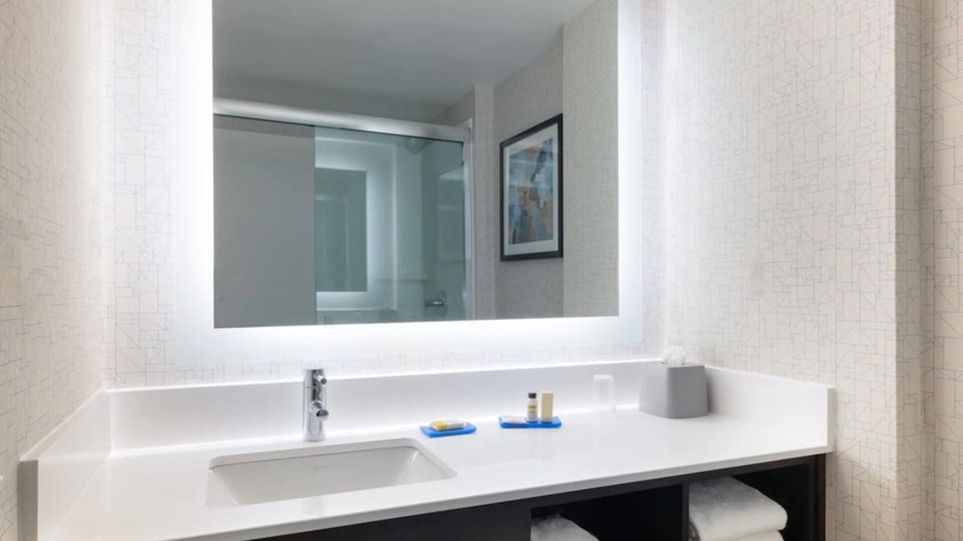Modern guest bathroom featuring a spacious vanity, illuminated mirror, premium toiletries, and fresh towels at Holiday Inn Express & Suites Boston-Cambridge.
