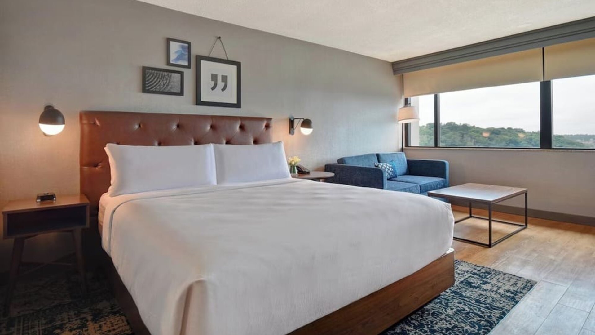 Contemporary king guest room offering plush bedding, comfortable seating, and expansive views through large picture windows at Four Points by Sheraton Boston-Newton.