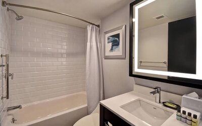 Modern guest bathroom featuring a sleek vanity, illuminated mirror, premium bath amenities, and a tub-shower combination at Four Points by Sheraton Boston-Newton.
