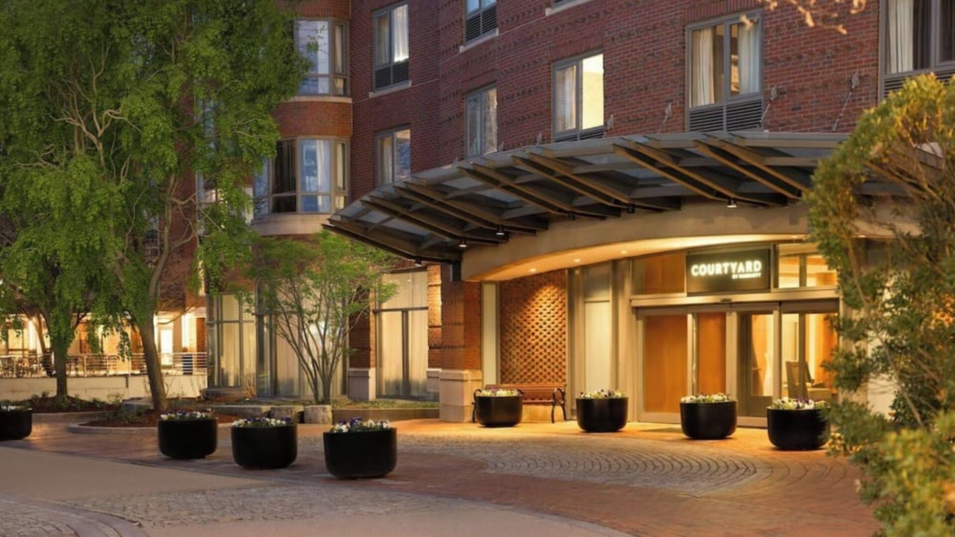 Welcoming hotel entrance featuring covered access, landscaped surroundings, and convenient arrival accommodations at Courtyard by Marriott Boston Brookline.