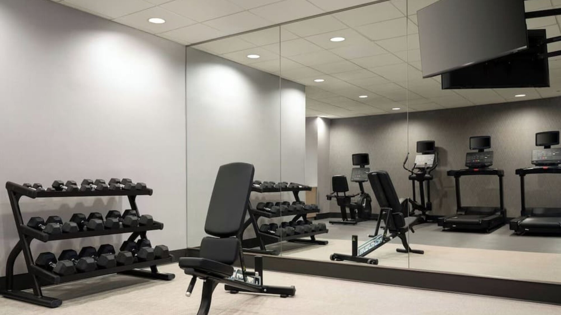 Well-equipped fitness facility with free weights, cardio machines, and mirrored workout spaces designed to support guests’ wellness routines at Courtyard by Marriott Boston Brookline.