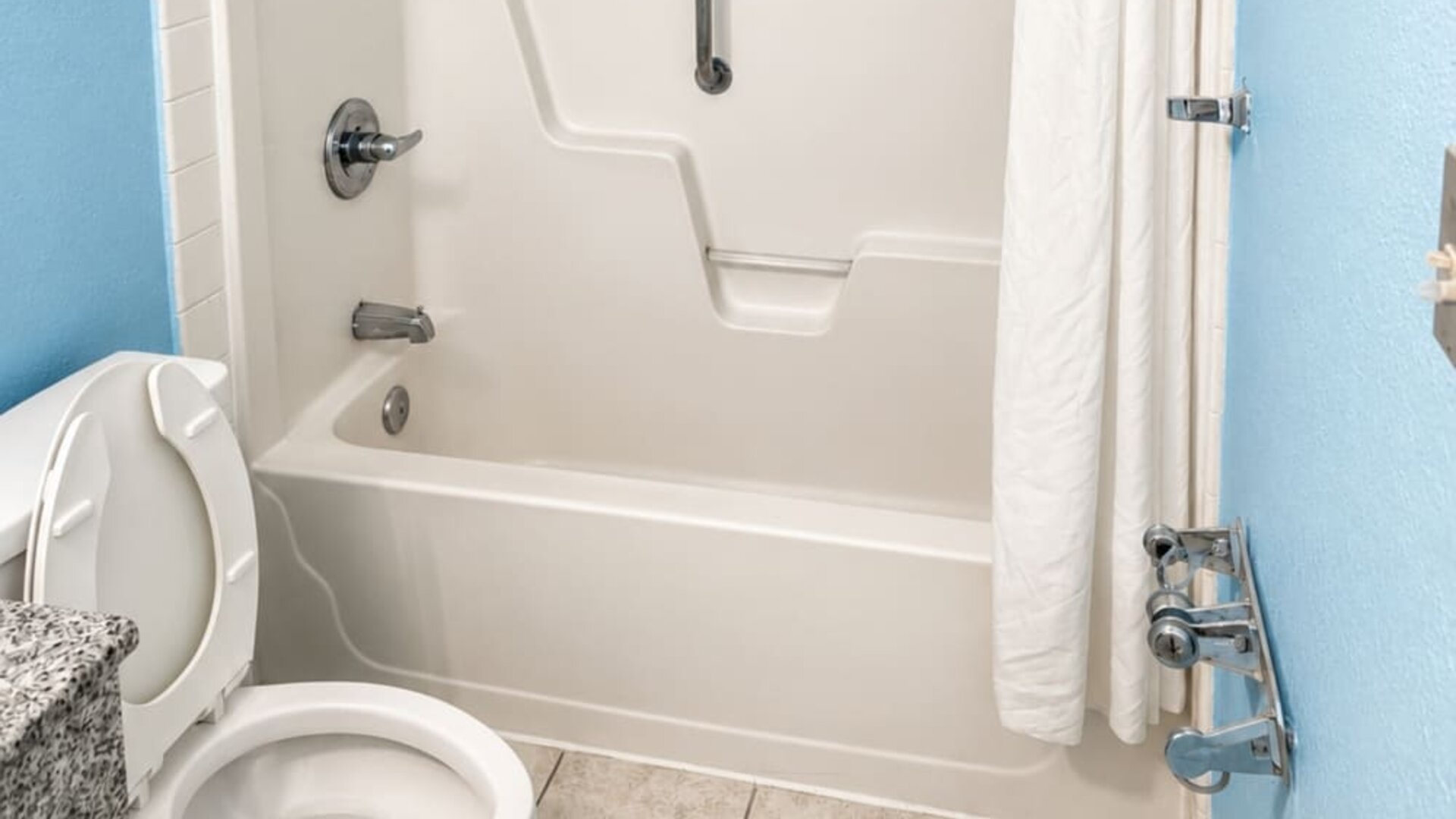Accessible guest bathroom featuring a tub-shower combination, safety grab bars, and mobility-friendly design elements for enhanced comfort at Blue Way Inn & Suites Wichita East.