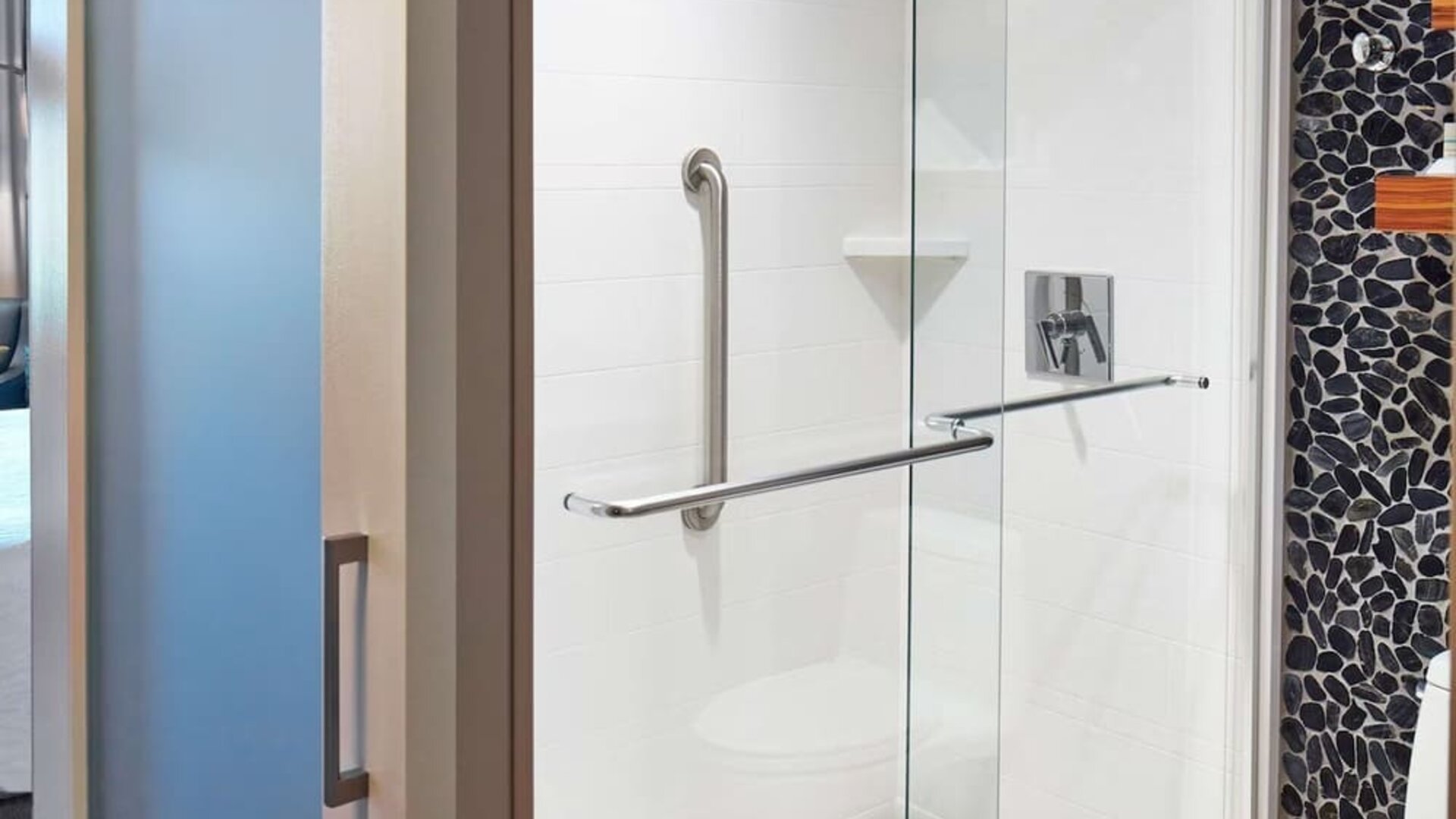 Accessible walk-in shower featuring glass enclosure, safety grab bars, and modern design elements for a comfortable and convenient stay at Hilton Garden Inn Boston/Marlborough.