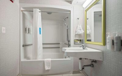 Accessible guest bathroom featuring a roll-in shower, support grab bars and modern vanity at Hampton Inn Ridgefield Park.