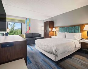 Spacious king guest room featuring contemporary furnishings, a comfortable sofa, ergonomic workspace, and premium bedding for a restful stay.