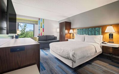 Spacious king guest room featuring contemporary furnishings, a comfortable sofa, ergonomic workspace, and premium bedding for a restful stay.