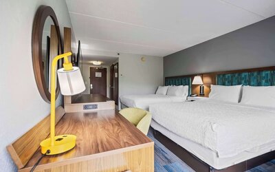 Double Queen guest room featuring two plush Hampton beds, a spacious work desk, comfortable seating, modern furnishings, and thoughtful amenities for a relaxing stay at Hampton Inn Ridgefield Park.
