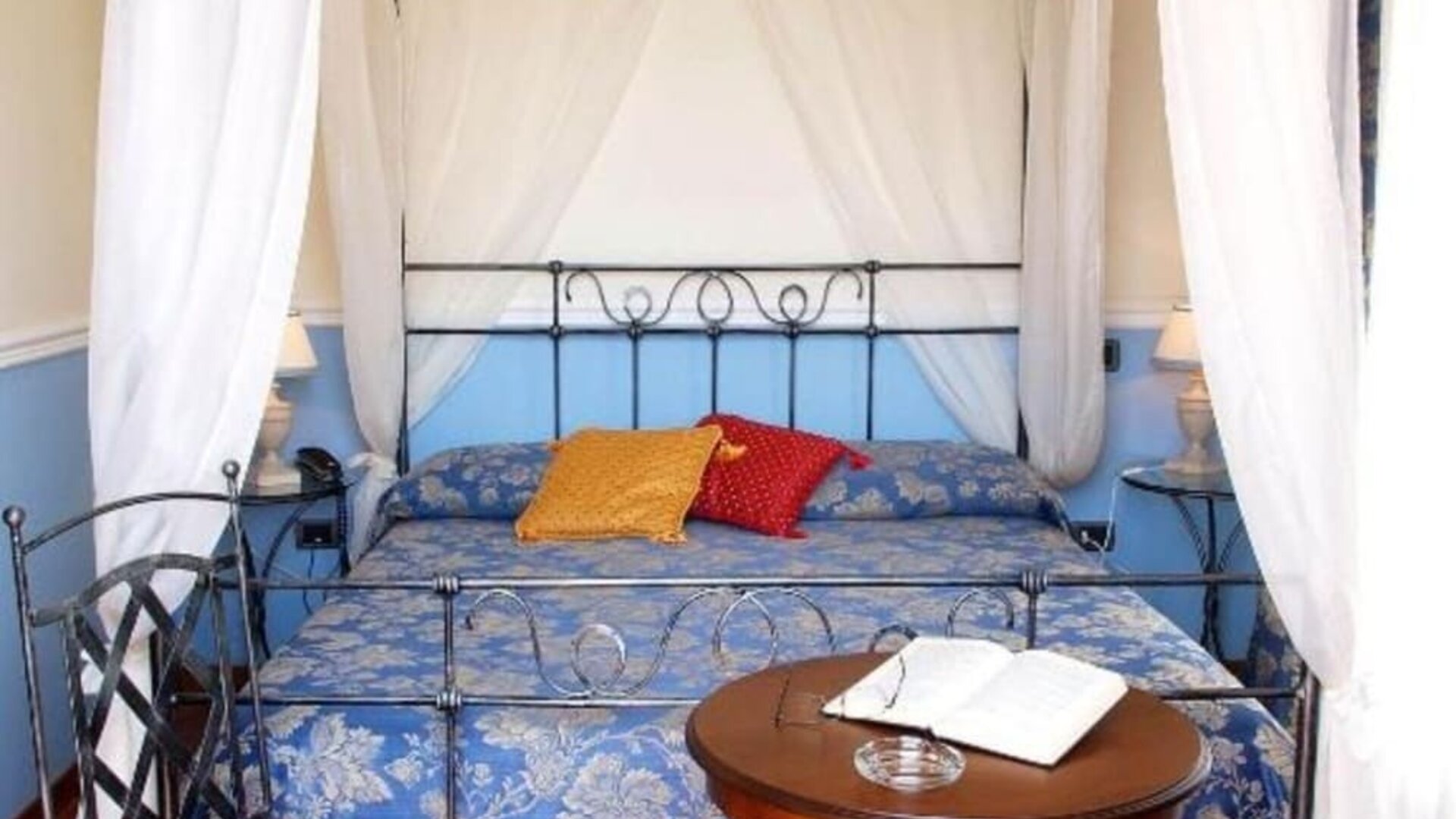 Romantic guest room with a wrought-iron canopy bed, hardwood flooring, and timeless décor.