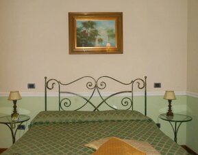 Comfortable guest room with a wrought-iron bed, soft green accents, and classic Italian styling.