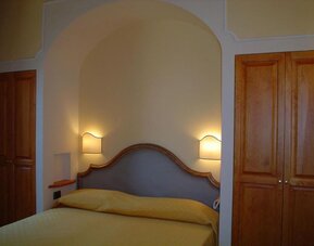 Cozy guest room with a double bed, upholstered headboard, built-in wardrobe, and warm ambient lighting.