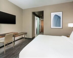 Modern guest room featuring a plush king bed, dedicated workspace, wall-mounted TV, contemporary furnishings, and a bright, minimalist design.