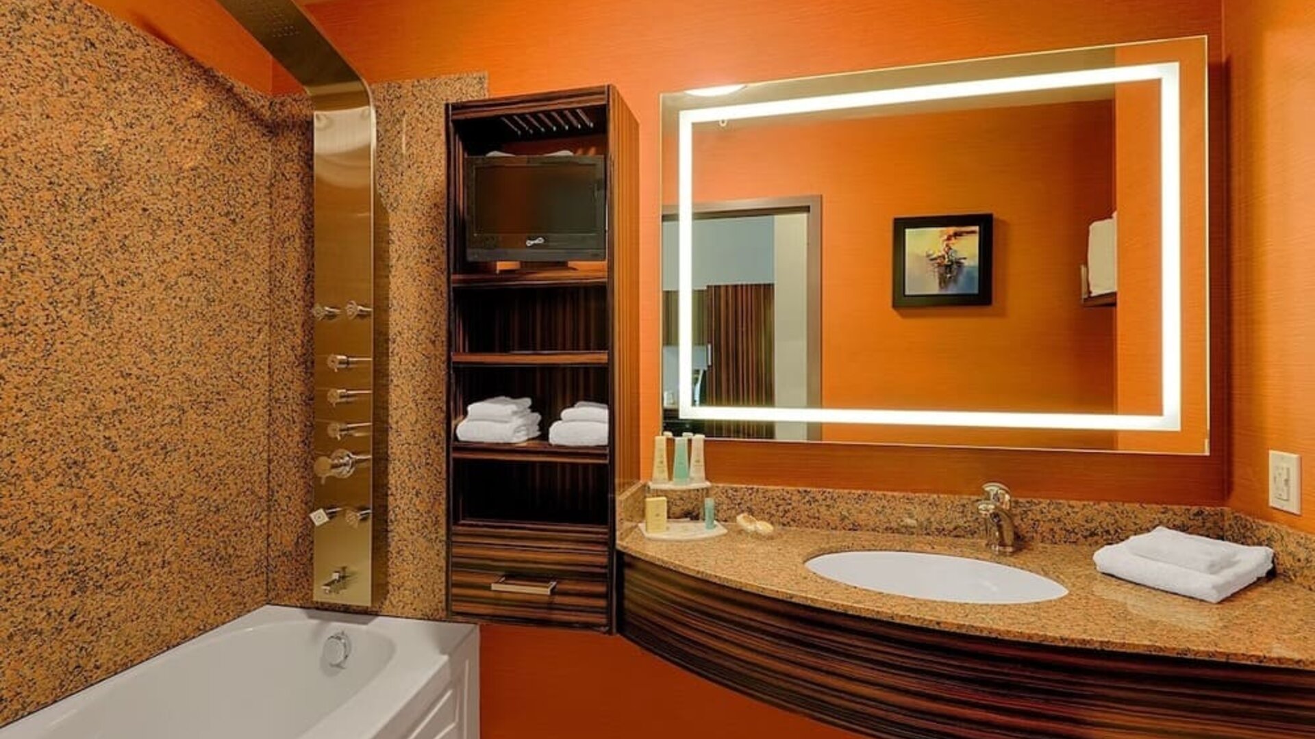 Bathroom with soaking tub, rainfall shower panel, illuminated mirror, granite vanity, and open shelving. Hotel Clique Calgary Airport.