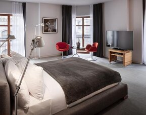 Spacious king guest room with large windows, red accent chairs, seating area, and flat-screen television. Hotel Gault.