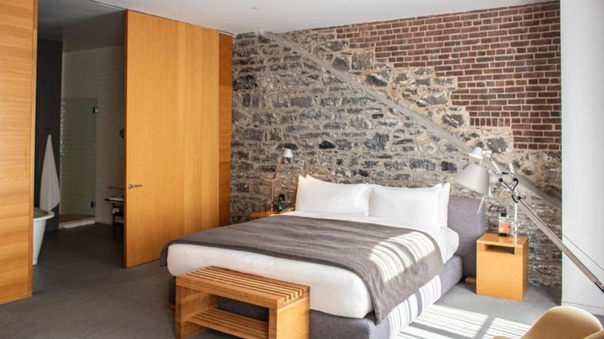 Guest room featuring an exposed stone and brick accent wall, king bed, and contemporary wooden furnishings. Hotel Gault.
