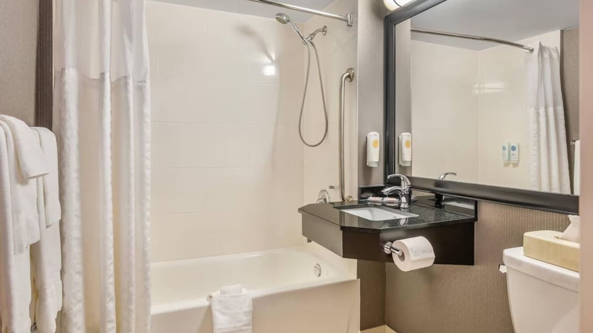 Accessible bathroom with bathtub and shower combination, grab bars, floating vanity, and large framed mirror at Comfort Inn Boucherville.