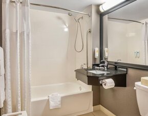 Accessible bathroom with bathtub and shower combination, grab bars, floating vanity, and large framed mirror at Comfort Inn Boucherville.
