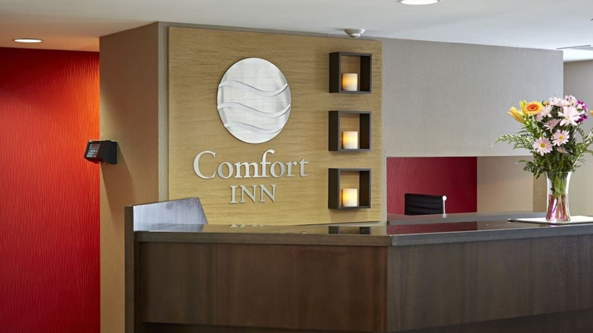 Reception desk with Comfort Inn logo, fresh flowers, and modern accent lighting behind the front counter at Comfort Inn Boucherville.