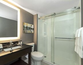 Modern bathroom with illuminated mirror, walk-in glass shower, black vanity, and fresh towels at Comfort Inn Boucherville.