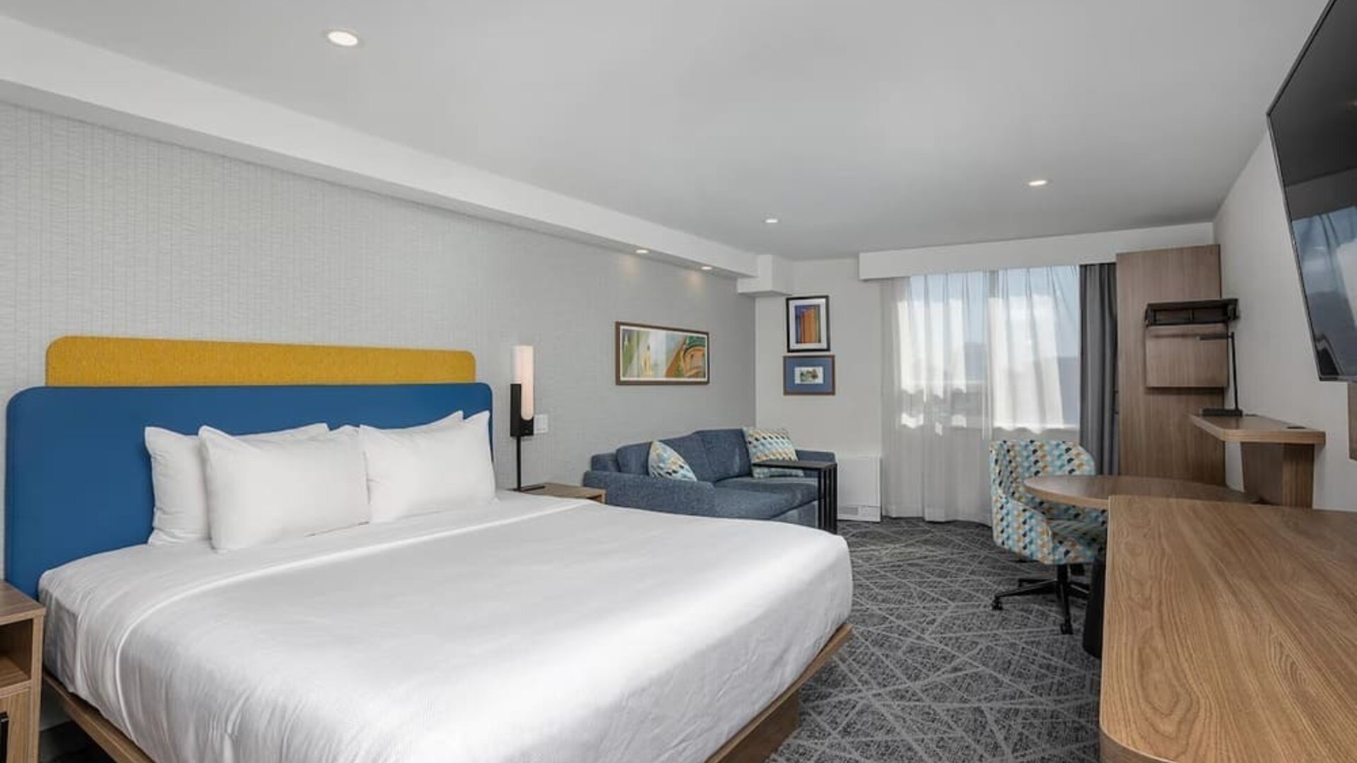 Spacious king guest room with sofa, work desk, and large television at Hampton Inn By Hilton Montreal East Anjou.
