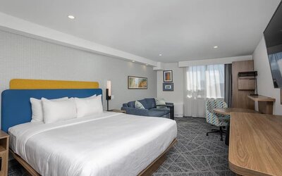 Spacious king guest room with sofa, work desk, and large television at Hampton Inn By Hilton Montreal East Anjou.