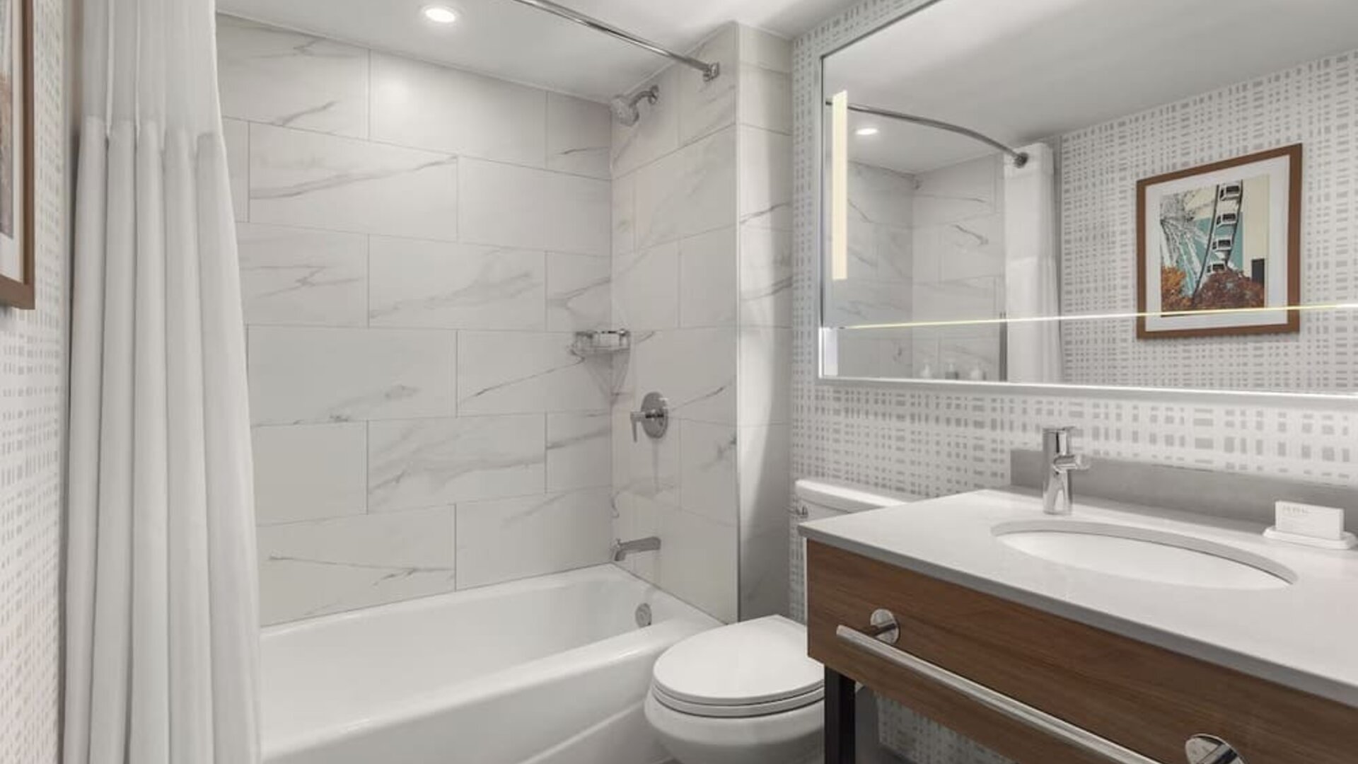 Modern bathroom with bathtub and shower combination, illuminated mirror, and wood vanity at Hampton Inn By Hilton Montreal East Anjou.