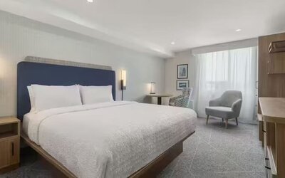 Spacious king guest room with seating area, work desk, large window, and contemporary furnishings at Hampton Inn By Hilton Montreal East Anjou.