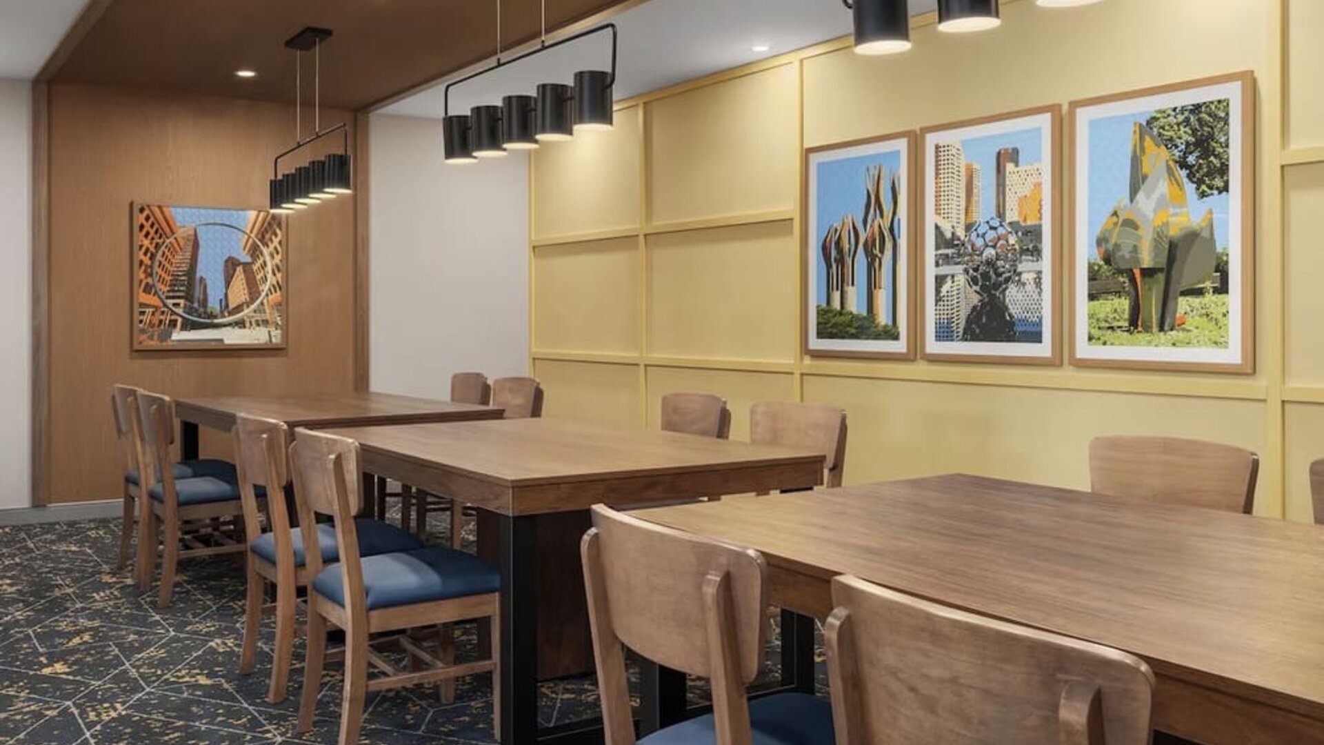 Dining area with communal tables, framed artwork, and modern pendant lighting at Hampton Inn By Hilton Montreal East Anjou.