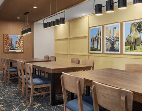 Dining area with communal tables, framed artwork, and modern pendant lighting at Hampton Inn By Hilton Montreal East Anjou.
