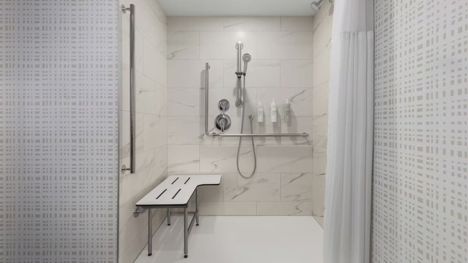 Accessible roll-in shower with grab bars, fold-down seat, and handheld showerhead at Hampton Inn By Hilton Montreal East Anjou.