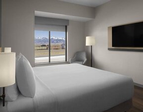 King guest room with mountain views, lounge chair, and wall-mounted television at Hyatt Place Bozeman Yellowstone Airport.
