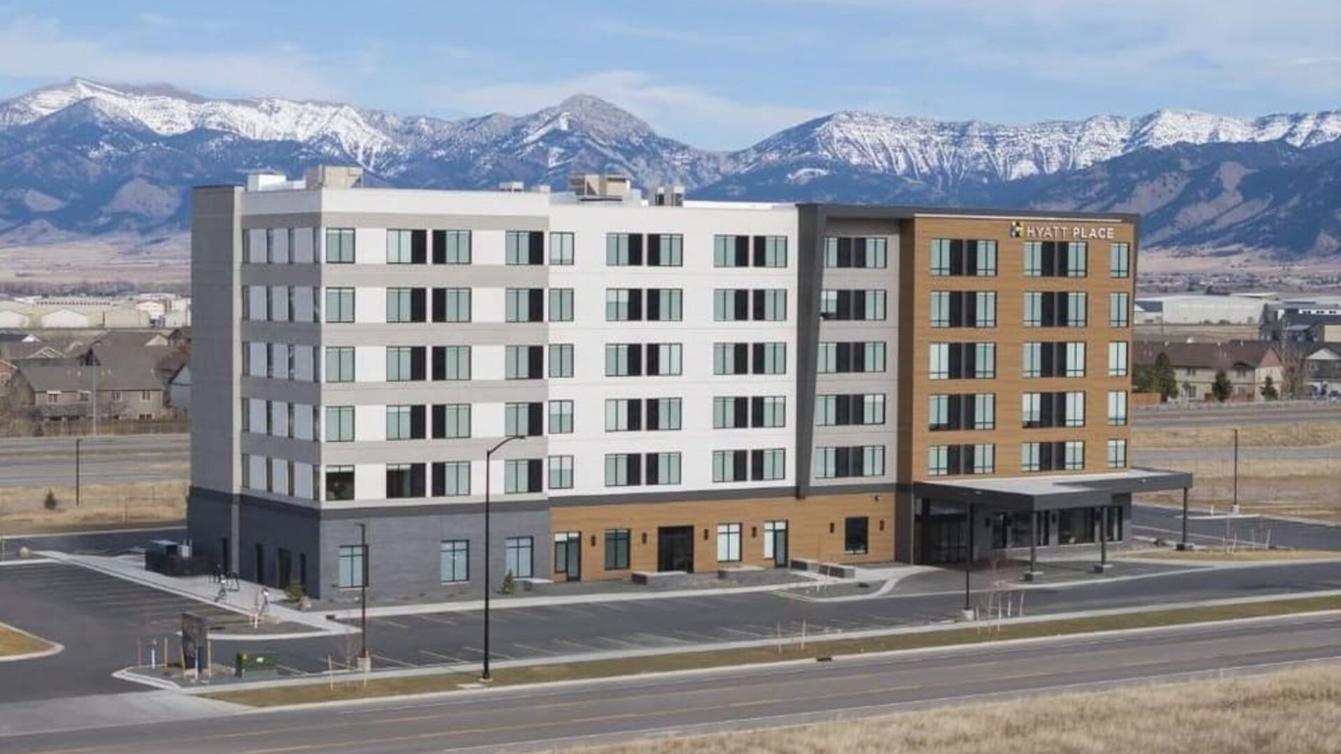 Modern hotel exterior with mountain backdrop and covered entrance at Hyatt Place Bozeman Yellowstone Airport.