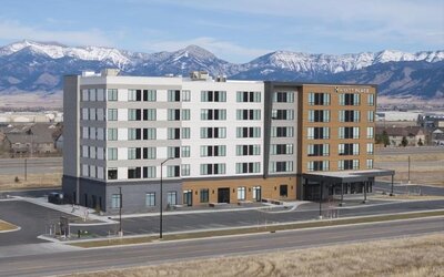 Modern hotel exterior with mountain backdrop and covered entrance at Hyatt Place Bozeman Yellowstone Airport.