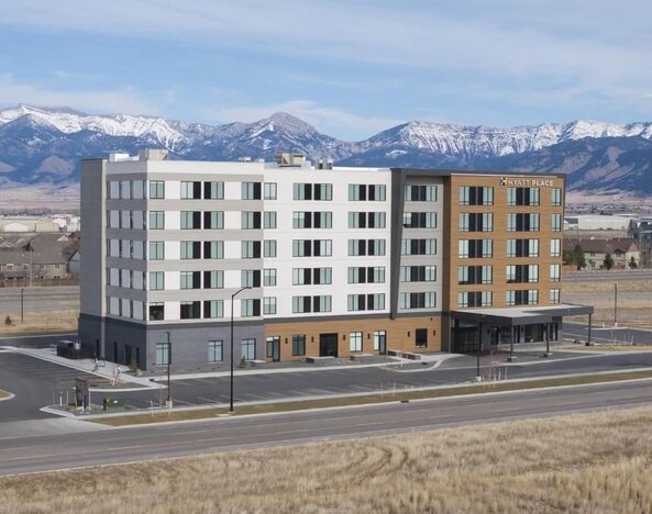 Modern hotel exterior with mountain backdrop and covered entrance at Hyatt Place Bozeman Yellowstone Airport.