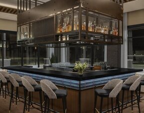 Contemporary hotel bar with wraparound seating, suspended liquor display, and elegant lighting at Hyatt Place Bozeman Yellowstone Airport.