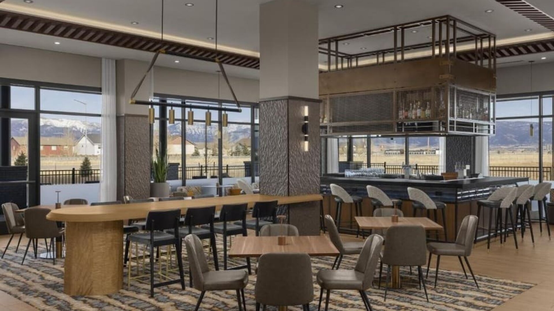 Modern dining area with communal tables, stylish bar seating, and floor-to-ceiling windows at Hyatt Place Bozeman Yellowstone Airport.
