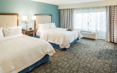 Spacious guest room with two queen beds, work desk, and large window at Hampton Inn & Suites Orlando at SeaWorld.
