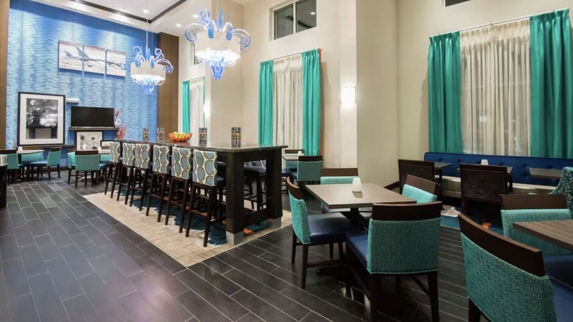 Bright dining area with communal seating, high-top tables, and contemporary décor at Hampton Inn & Suites Orlando at SeaWorld.