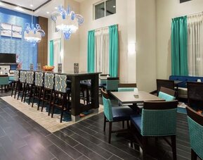Bright dining area with communal seating, high-top tables, and contemporary décor at Hampton Inn & Suites Orlando at SeaWorld.