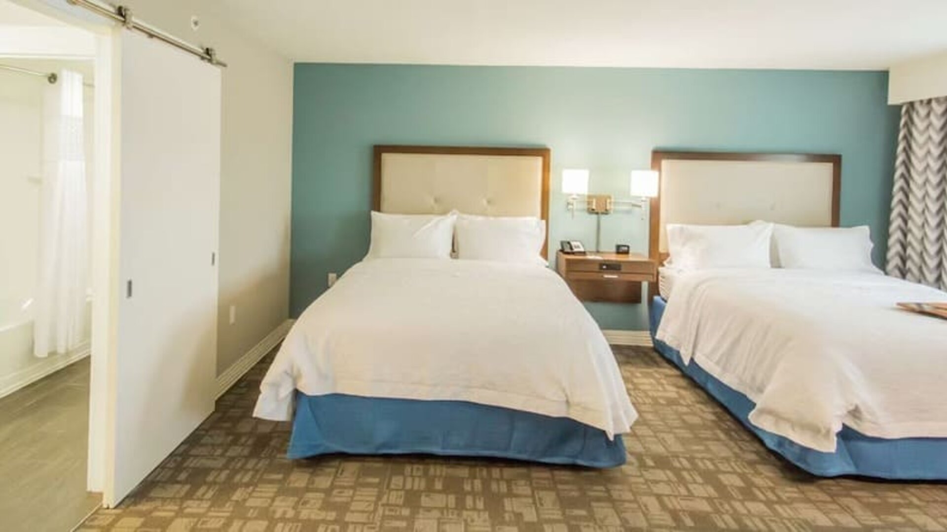 Guest room with two queen beds, spacious layout, and accessible bathroom entrance at Hampton Inn & Suites Orlando at SeaWorld.