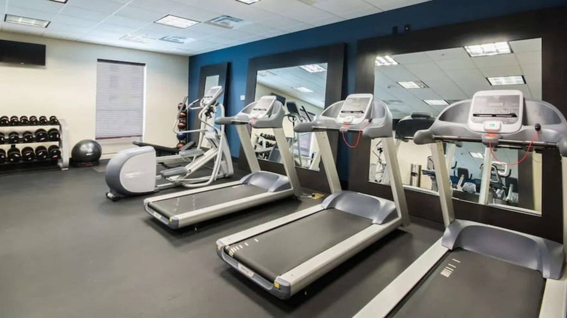 Fitness center with treadmills, cardio machines, free weights, and mirrored wall at Hampton Inn & Suites Orlando at SeaWorld.
