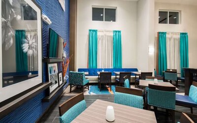 Lobby lounge with dining tables, seating area, and high ceilings at Hampton Inn & Suites Orlando at SeaWorld.