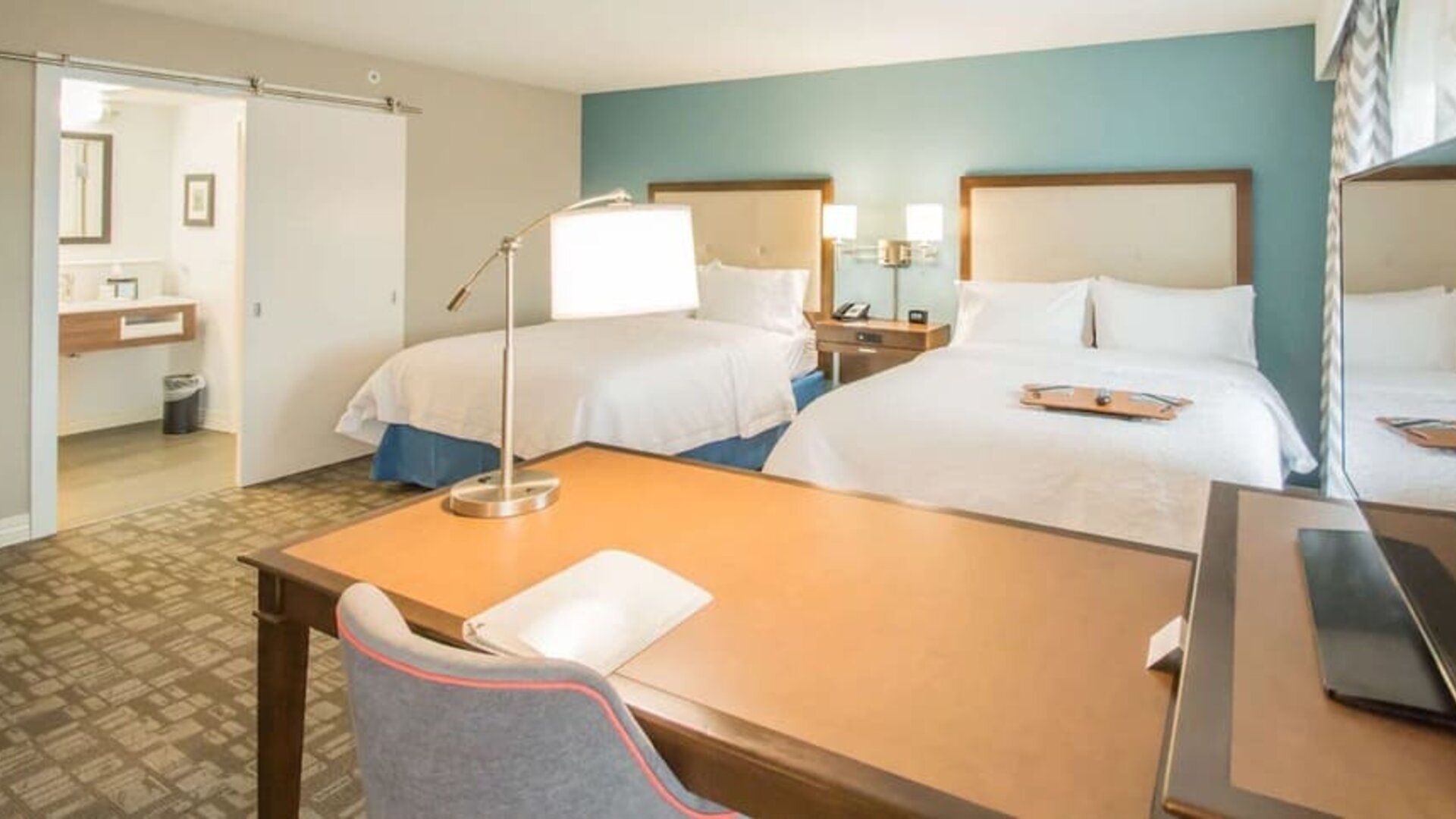 Guest room with two queen beds, work desk, and vanity area at Hampton Inn & Suites Orlando at SeaWorld.