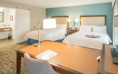 Guest room with two queen beds, work desk, and vanity area at Hampton Inn & Suites Orlando at SeaWorld.