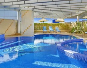 Covered outdoor pool with curved design, lounge chairs, shaded seating areas, and relaxing leisure space.