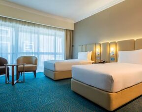 Comfortable twin-bed room with upholstered headboards, sitting area, floor-to-ceiling curtains, and soft ambient lighting.