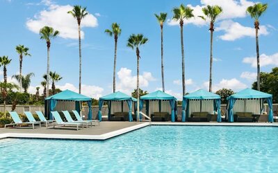 Outdoor swimming pool with turquoise cabanas, lounge chairs, palm trees, and sunny resort atmosphere.