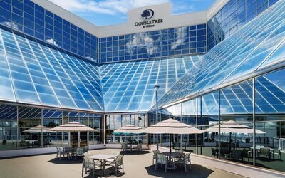Open-air terrace with patio tables, umbrellas, and glass hotel façade reflecting blue skies.