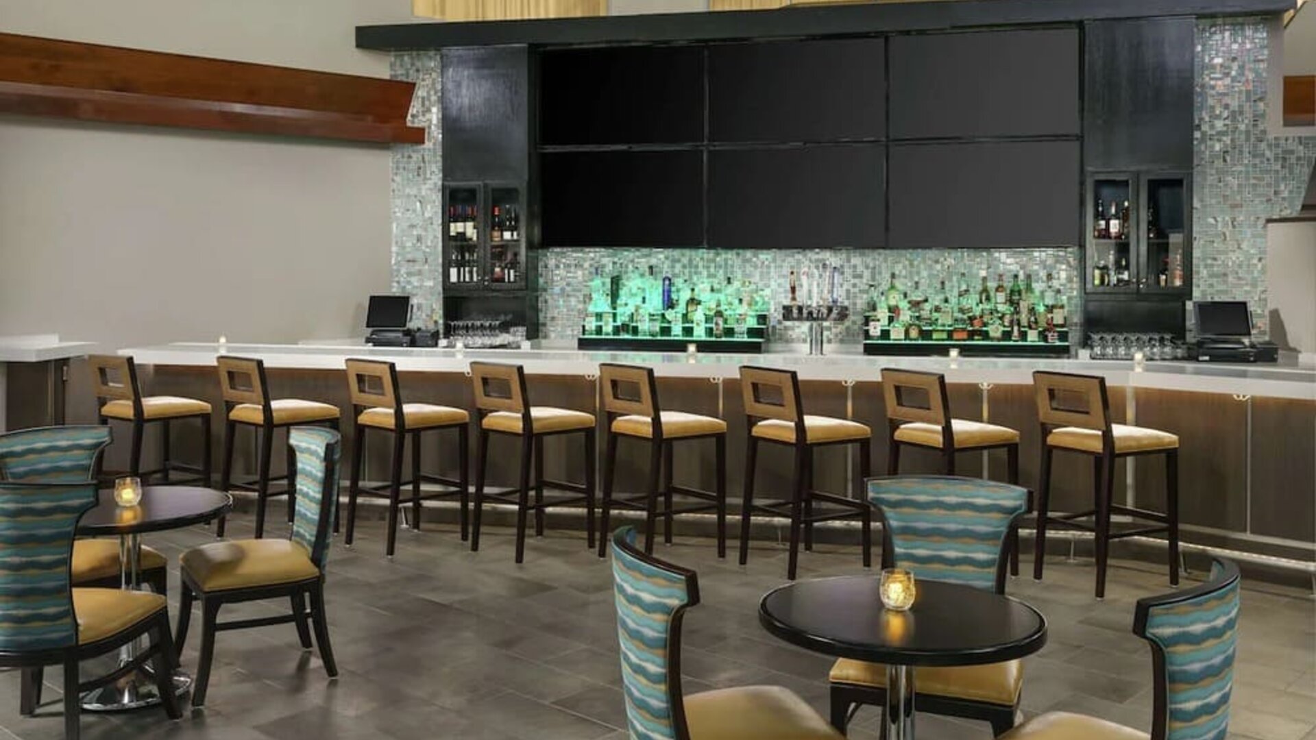 Stylish hotel bar with high-top seating, illuminated back bar, cocktail tables, and lounge-style chairs.