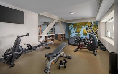 Modern fitness center featuring cardio machines, free weights, workout bench, and large windows.